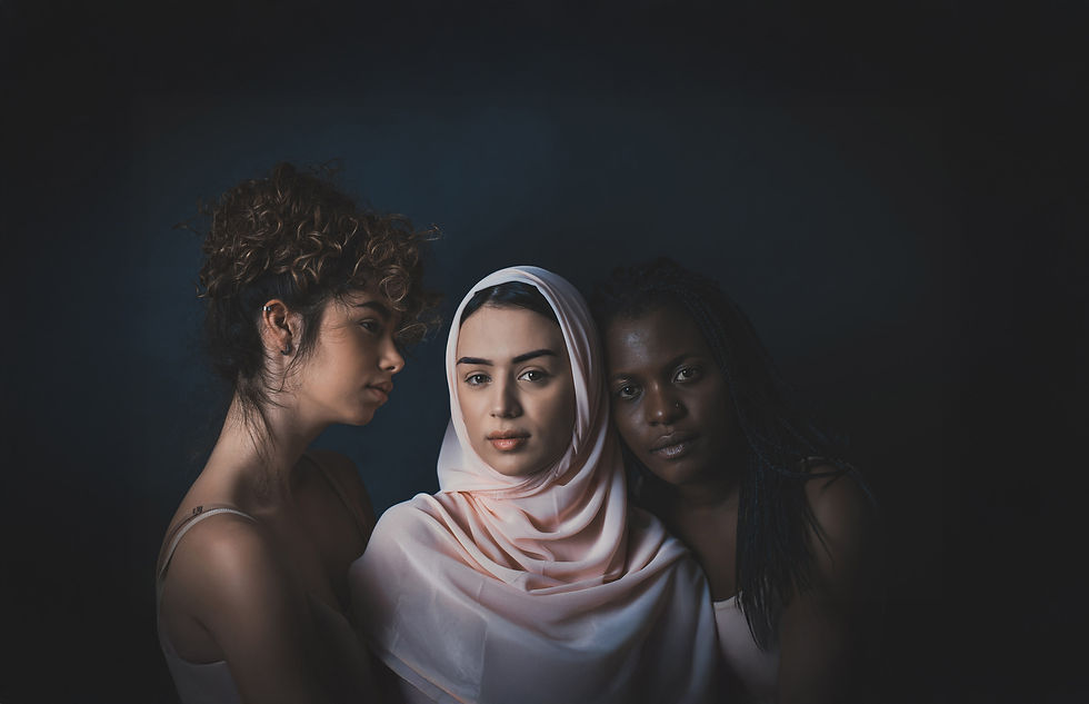 Portrait of three women of diverse backgrounds standing closely together against a dark background, conveying unity and solidarity.