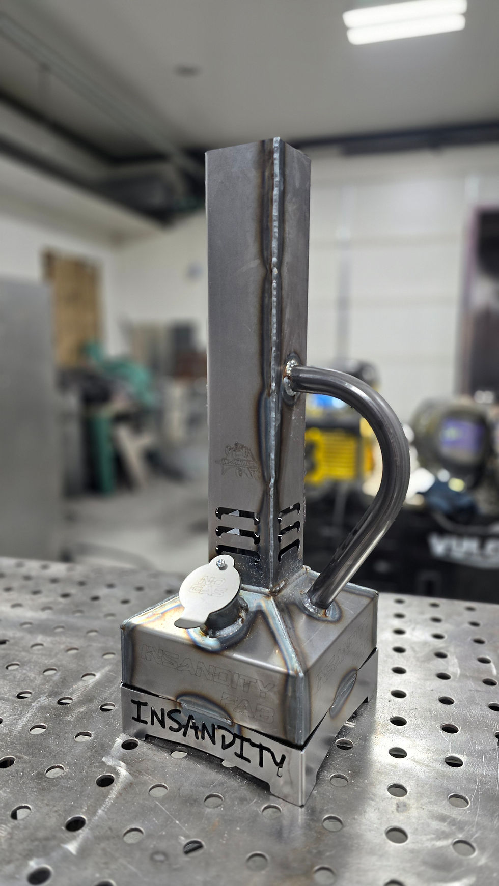 Smudge pot in color raw steel, sitting on a welding table in a metal working shop.