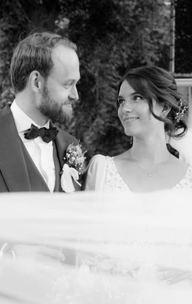 Ein Brautpaar steht nebeneinander und blickt sich tief in die Augen. Der Schleier der Braut weht im Wind.