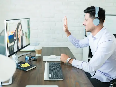 A remote sales professional with headphones participating in a video conference with a diverse team on a computer screen, highlighting how nearshore staffing helps companies scale fast in their time zone.