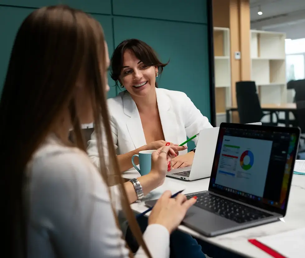Two businesswomen collaborate in a modern office, reviewing sales performance data on a laptop, illustrating a successful partnership that scales revenue with the complete guide to sales outsourcing from Confetti Recruitment.