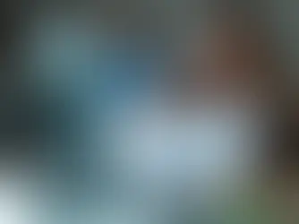 A focused female sales development representative (SDR) in glasses with a pen reviews documents at her desk, with a desktop computer and colleagues in the background, illustrating the meaning of an SDR in sales building a revenue machine.