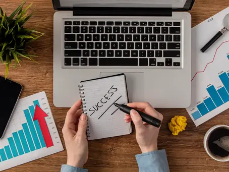 A person's hands are visible on a wooden desk, writing "SUCCESS" in a notebook. This is part of the confetti recruitment process for SDR vs AE positions, helping businesses scaling their sales teams.