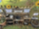 An outdoor mud‑kitchen play station made from wooden crates and pallets, with pots, pans, shells, and natural materials arranged beneath gardening‑themed signs and decorations