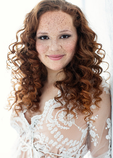 Smiling woman with curly red hair and freckles in a lace robe, beauty portrait
