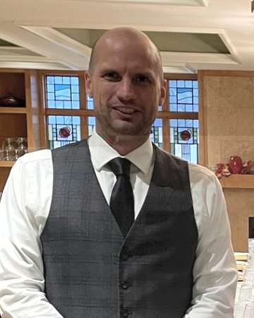 Mark Regensburg in a grey vest and tie in a dining room set for an event