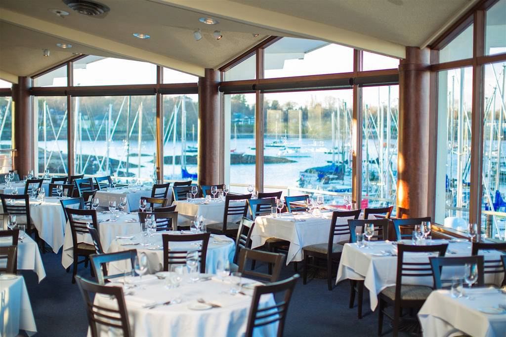 The Seaside Room set with white-linen tables, facing tall windows over the boats of Oak Bay Marina