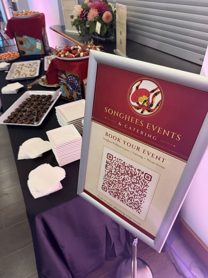 A Songhees Events & Catering Book Your Event sign with the octopus logo beside a reception buffet of canapés and desserts
