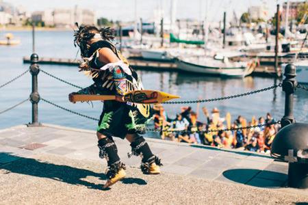 A dancer in traditional regalia performing on the waterfront at Victoria's Inner Harbour as a crowd looks on