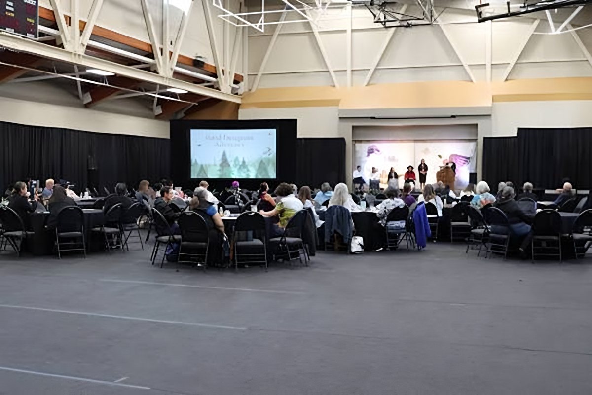 He'was Hall set for a conference, with guests at round tables facing a stage and a large presentation screen