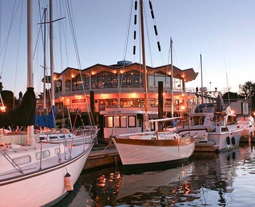 Oak Bay Marina restaurant lit up at dusk behind moored sailboats