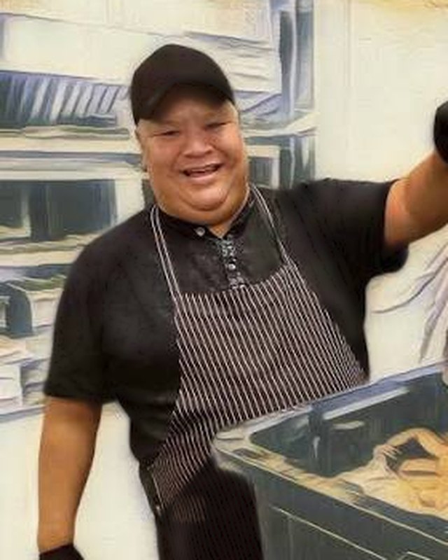 Aaron George in a black cap and striped apron, smiling in the kitchen