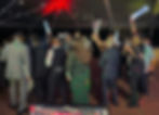 High-energy event crowd dancing with white LED foam glow sticks under green club laser light effects on a packed dance floor.