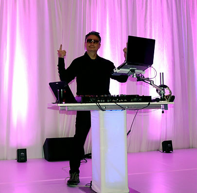 Professional event DJ standing at an illuminated booth mixing music under elegant pink ven
