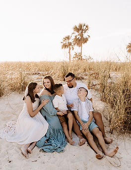 Family of 5 sitting at the beach snuggling in the sand during a family portrait session in Central Florida.
