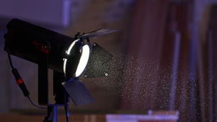 Spotlight projecting bright light, illuminating floating dust in a dim room with wooden planks. Black and red details on the light.