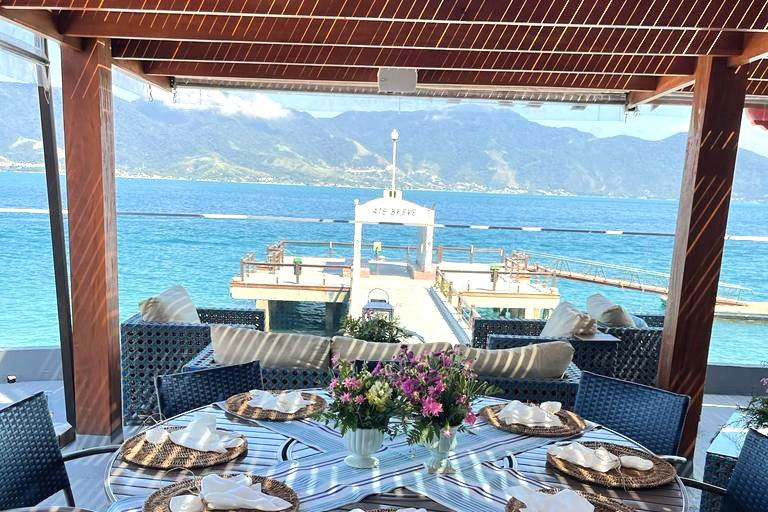 Vista panorâmica de Ilhabela com destaque para o mar e a natureza exuberante, sugerindo um ambiente propício à gastronomia. Pode incluir um barco de pesca artesanal ao longe.