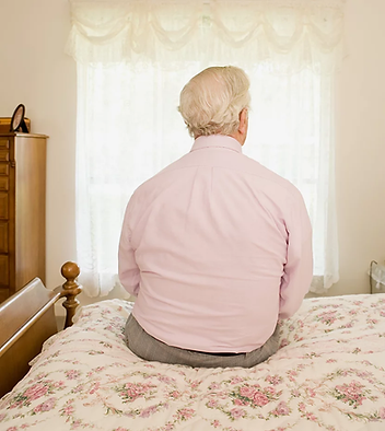 Lonely elderly man sitting on the bed in his room.