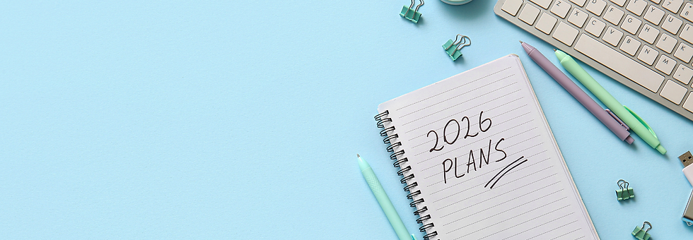 Notebook on blue desk with "2026 PLANS" written. Nearby are pens, binder clips, keyboard, and a USB drive, creating a productive mood.