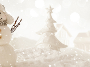 Festive snowman with a scarf and hat, twig arms, and button eyes in a snowy scene with blurred houses and a tree in the background. Bright and cheerful.