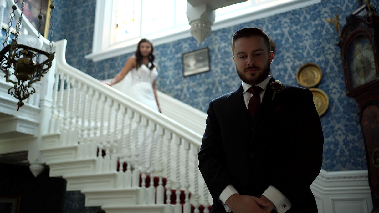 the bride ascends a white stair case where her fiance is waiting for her at the bottom in anticipation for the first look