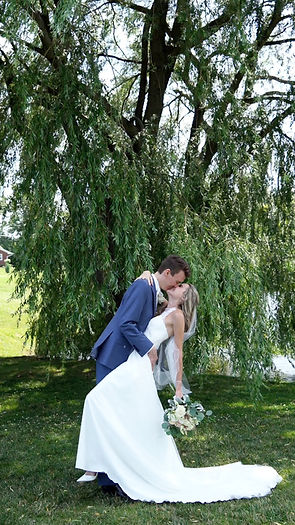 groom kissing bride and dipping her while she holds the bouquet back in her left hand. Both smiling underneath a willow tree in Buffalo NY