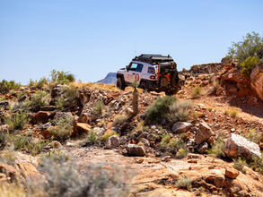 A white FJ Cruiser from Four Points Adventures on a rocky dirt trail on the Grand Canyon's North Rim. The blue sky highlights the vehicle surrounded by rocks and desert flora.
