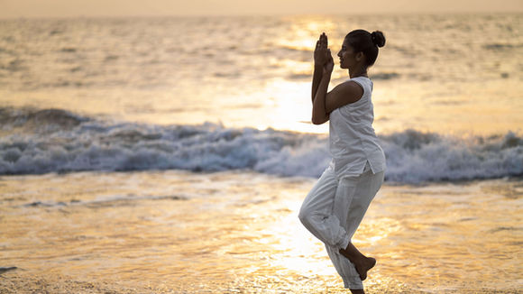 Guest practising yoga by the beach at sunrise at Nattika Beach Ayurveda Resort in Kerala.