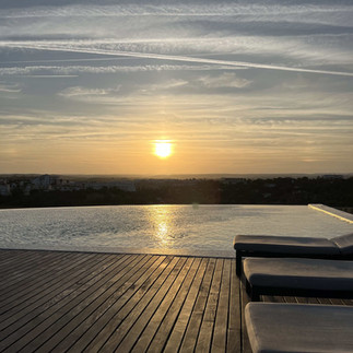 Rooftop pool at sunset with views of the Algarve and sunbeds along a wooden deck.