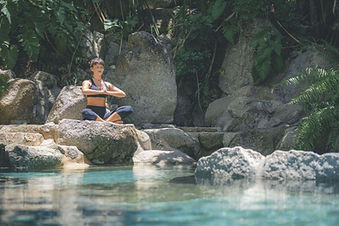 Woman meditating by natural rock pool at Kamalaya Koh Samui