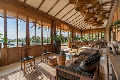 Natural, serene interior of Rakxa Integrative Wellness retreat, featuring wooden furnishings, woven baskets, and large windows overlooking lush greenery and a calm waterway.