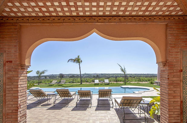View from under a terracotta arch at Al Karob Boutique Hotel, overlooking sun loungers and the outdoor pool surrounded by greenery in Portugal’s Algarve region.