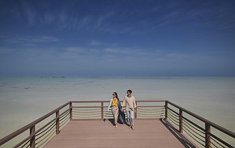 Couple walking on a deck overlooking the serene beach at Zulal Wellness Resort