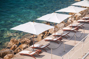 Beachfront sun loungers and white umbrellas beside the crystal-clear Adriatic Sea at Sun Gardens Dubrovnik.