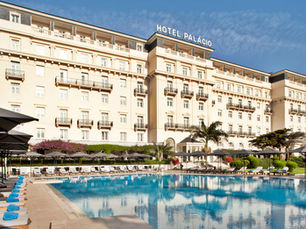 Elegant exterior of Palácio Estoril Hotel in Portugal, with a large outdoor swimming pool, sun loungers, and classic architectural design