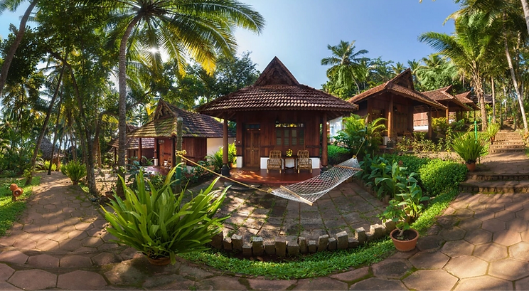 Traditional wooden cottages surrounded by lush tropical gardens and palm trees with a hammock outside at Somatheeram Ayurveda Village in Kerala, India.