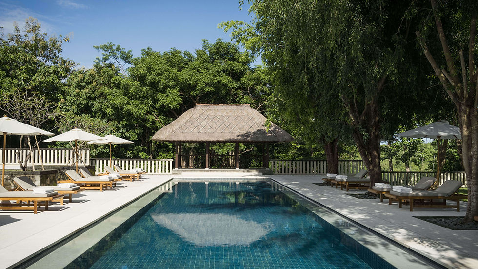 Peaceful pool area at REVĪVŌ Wellness Resort in Nusa Dua, Bali, surrounded by tropical trees and traditional thatched pavilion.