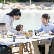 Family sharing a meal at a poolside table at Zulal Wellness Resort