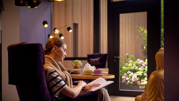 Guest relaxing with tea and a book in the lounge at Ayurveda Resort Mandira