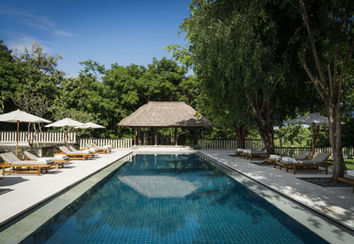 Serene pool area at REVĪVŌ Wellness Resort in Bali, surrounded by tropical trees, sun loungers, and a traditional thatched pavilion