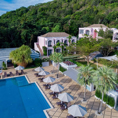Aerial view of Absolute Sanctuary in Koh Samui, Thailand, featuring a large swimming pool surrounded by sun loungers and parasols, with tropical greenery in the background.