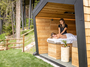 A serene spa retreat with a therapist massaging a guest in a wooden outdoor spa cabin nestled among tall trees