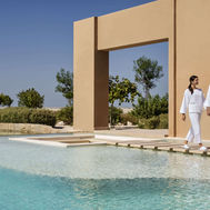 Couple walking along water pathway under modern arch at Zulal Wellness Resort