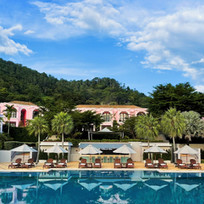 Aerial view of Absolute Sanctuary in Koh Samui, Thailand, featuring a large swimming pool surrounded by sun loungers and parasols, with tropical greenery in the background.