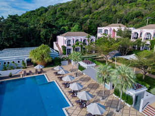 Aerial view of Absolute Sanctuary in Koh Samui, Thailand, featuring a large swimming pool surrounded by sun loungers and parasols, with tropical greenery in the background.