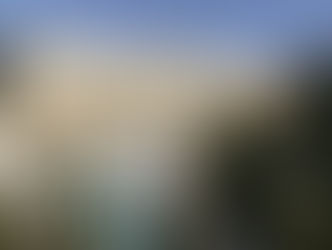 Palace Merano hotel with white balconies, palm trees, and a pool in the foreground. Mountain backdrop under a clear blue sky.