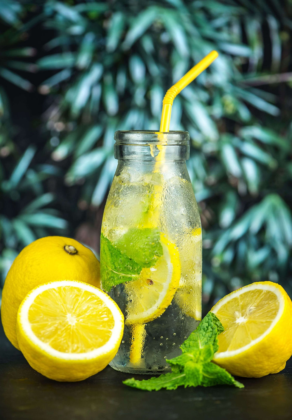 Glass of lemon and mint detox water with fresh citrus fruits in background.