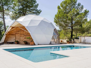 Mas Qi, The Energy House in Spain, featuring a white geodesic dome structure with a serene outdoor pool, set amidst a natural landscape of trees and clear skies.