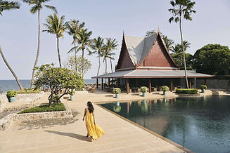 Woman walking along Chiva-Som’s oceanfront pavilion framed by palm trees