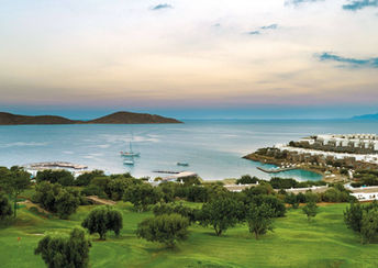 View of the private beach and turquoise bay at Porto Elounda in Crete, Greece, with sun loungers and lush Mediterranean surroundings